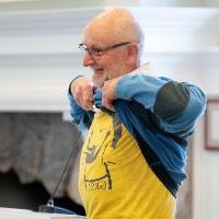 Man lifts up sweater to show yellow t-shirt underneath that says G.V.S.C.